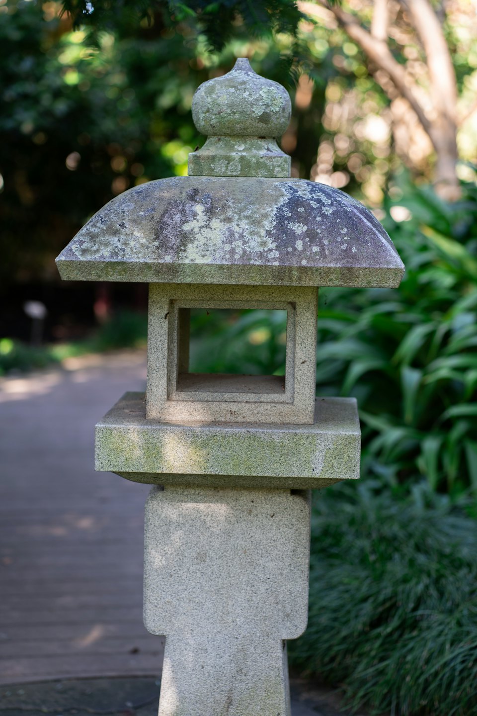 Verweerde stenen lantaarn in een weelderige groene tuin.